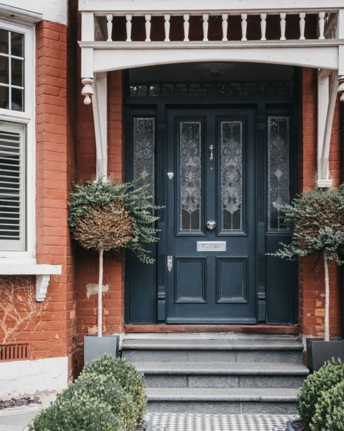 Victorian front door painted dark blue-grey with stained glass panels, white porch woodwork above and a tiled path leading up to it.